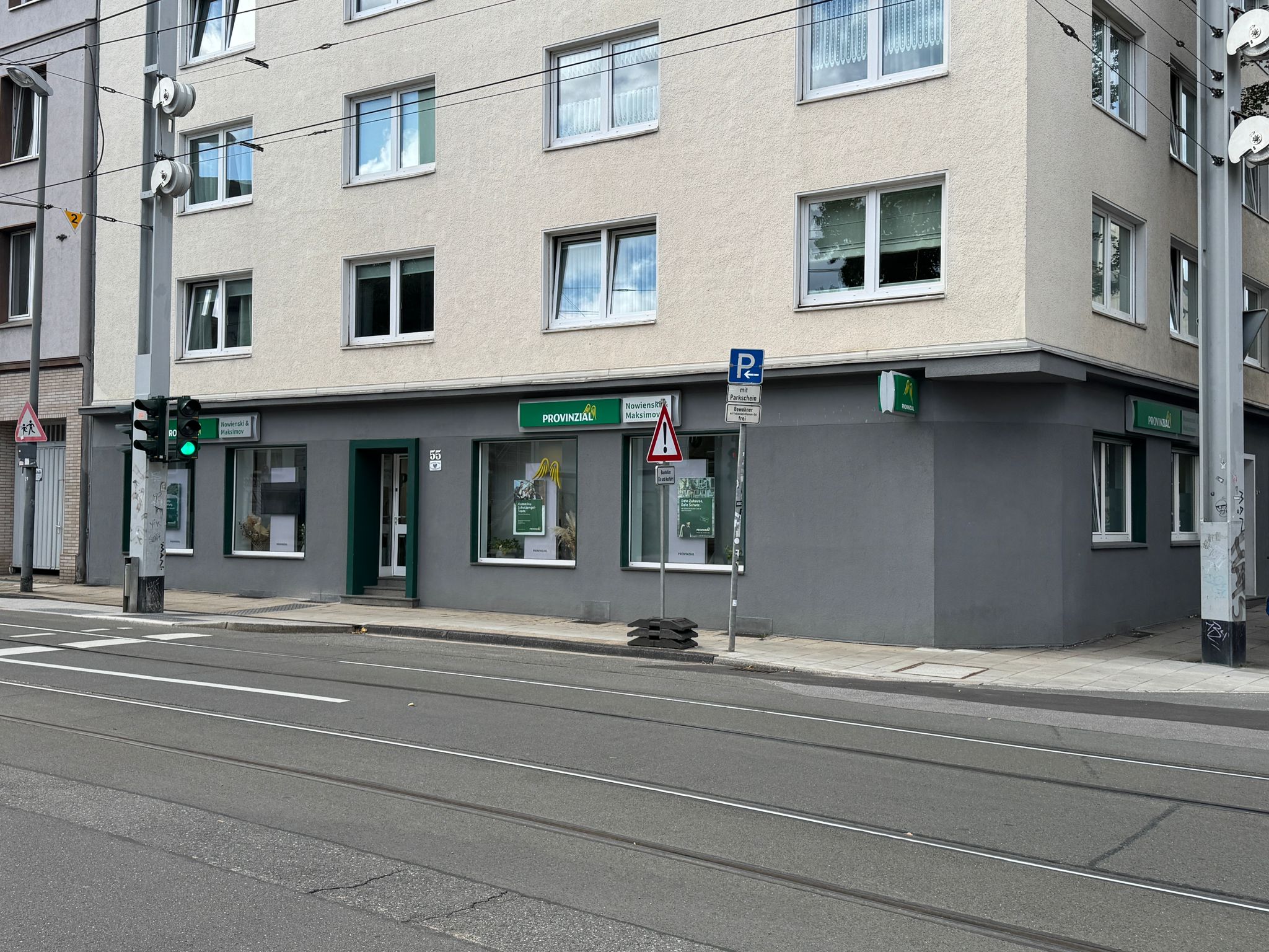 Ein graues Gebäude mit mehreren Fenstern, grüner Straßenschild und Ampel.