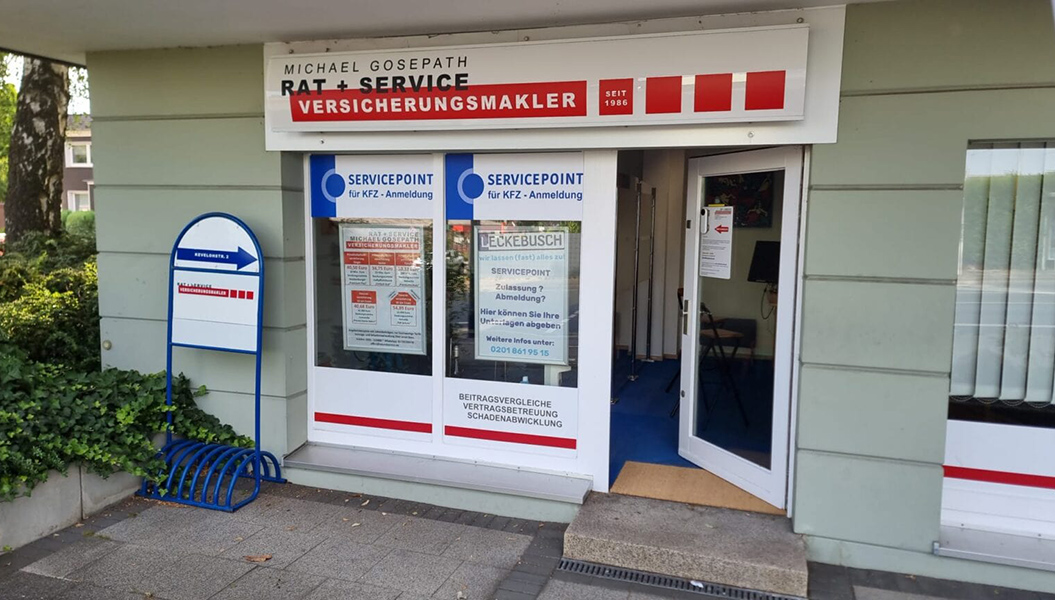Eingang zu einem Versicherungsbüro mit weißen und roten Schildern und Glasfront