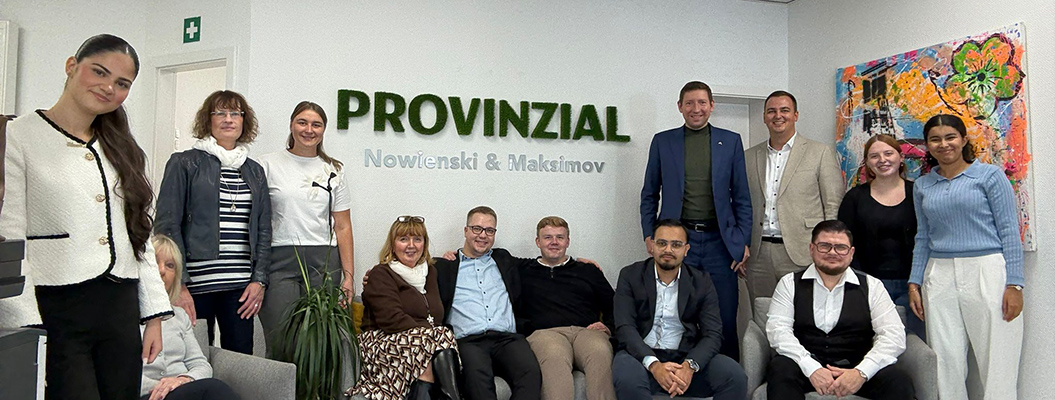 Eine Gruppe freundlich lächelnder Menschen steht vor einer weißen Wand mit grünem PROVINZIAL Schriftzug, im Hintergrund hängt ein farbenfrohes Gemälde