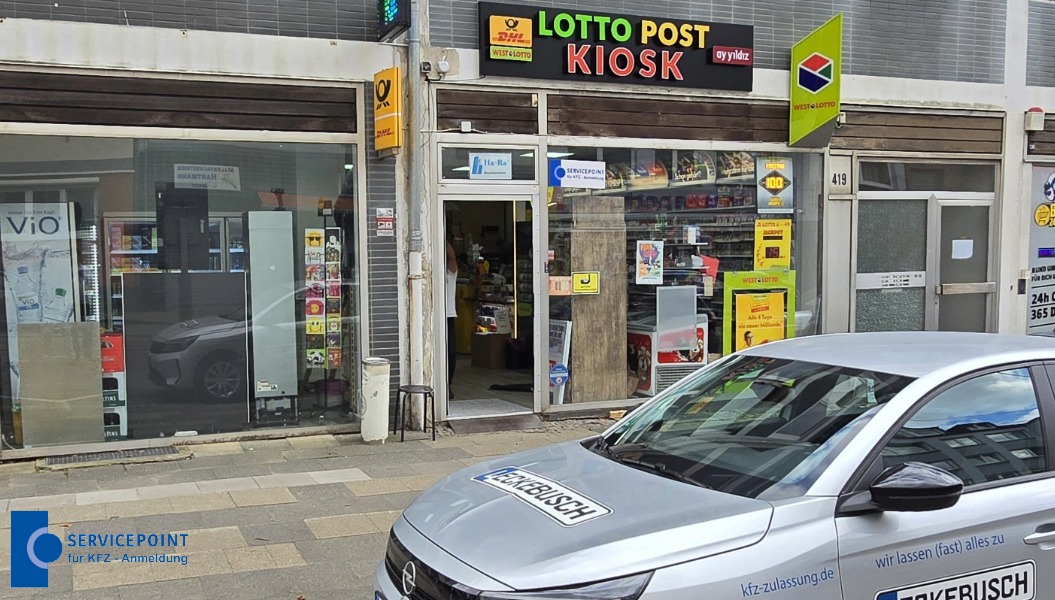 Ein Kiosk mit buntem Lotto Post Schild und einem silbernen Auto im Vordergrund