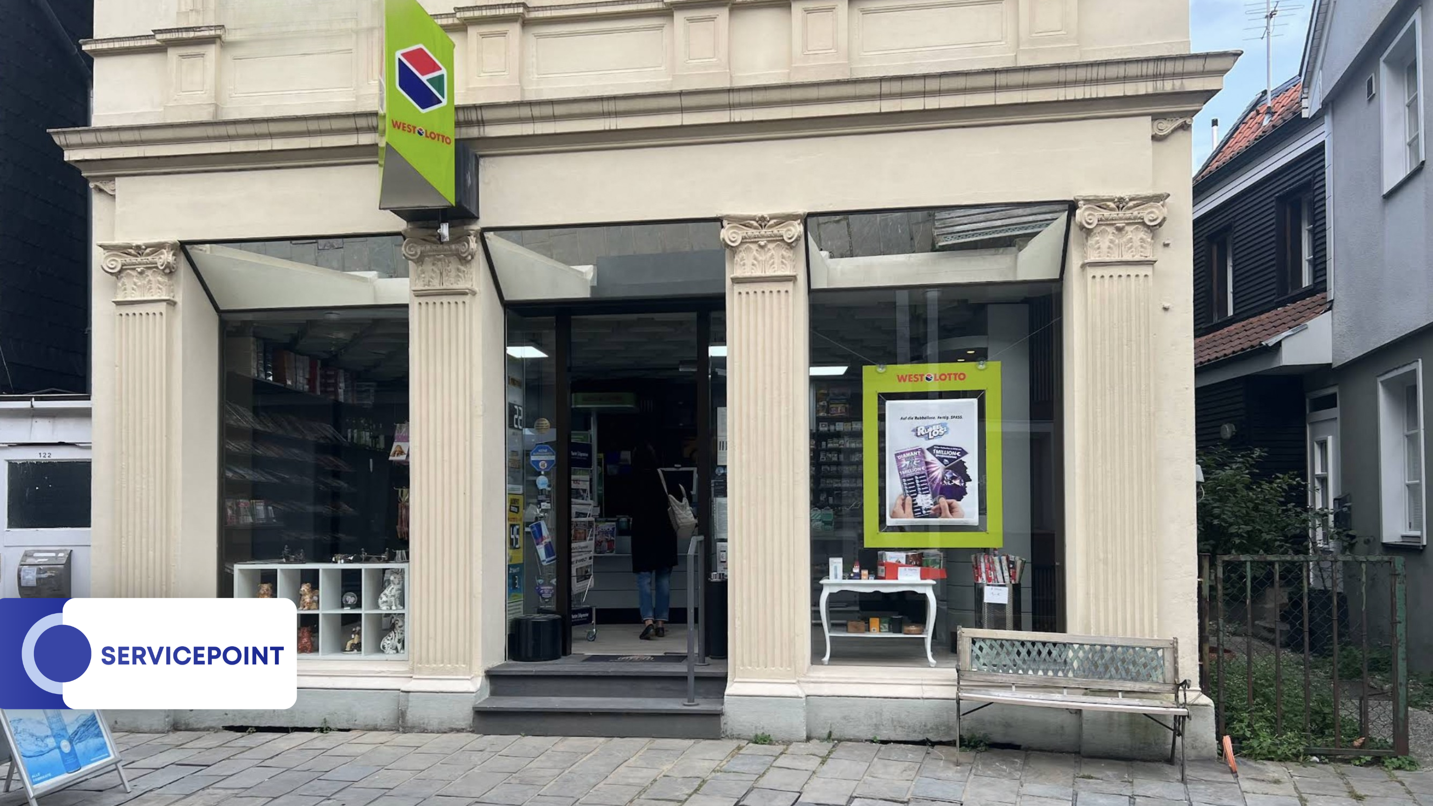 Person hinter Glas mit neutralem Blick im grauen Laden mit Säulen und Servicepoint Schild